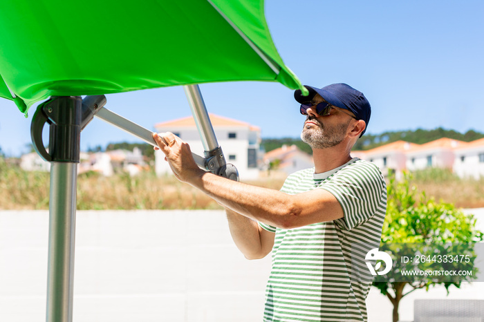 Mature man opening up a green parasol in the garden in a sunny day