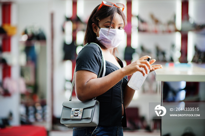 African american woman wearing face protective medical mask for protection from virus disease in shoes store use hand sanititzer during coronavirus pandemia.