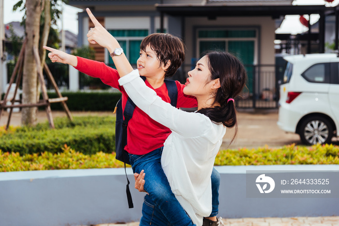 Asian family happy mother carrying and walking her kid, the kid point hand finger out outdoors, Back to home from school concept