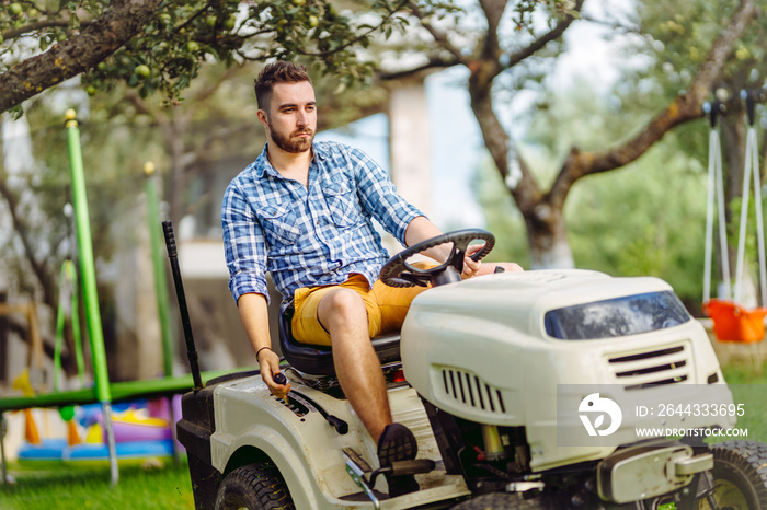 Man using lawn tractor for mowing grass in garden. Landscaping works with professional tools