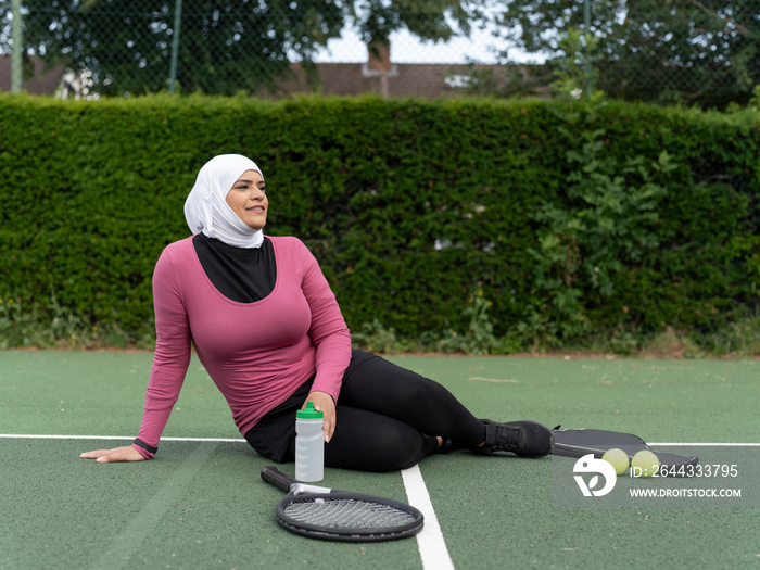 UK,Sutton,Woman in headscarf resting on tennis court