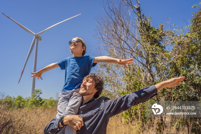 Alternative energy, wind farm and happy time with your family. Happy father carrying his son on shoulders is on vacation and escape to nature. Father carrying son on shoulders and waving their arms