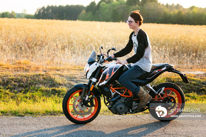 young boy driving motorycle without a helmit on a country road in the summer