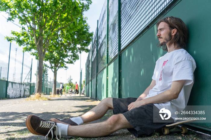 Young man sitting on skateboard outdoors