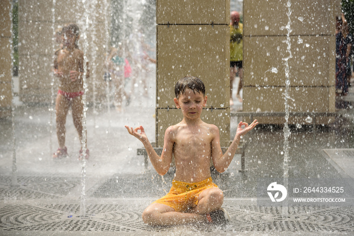 Boy meditating in water fountain find ZEN. Child playing with a city fountain on hot summer day. Happy kids having fun in fountain. Summer weather. Active leisure, lifestyle and vacation