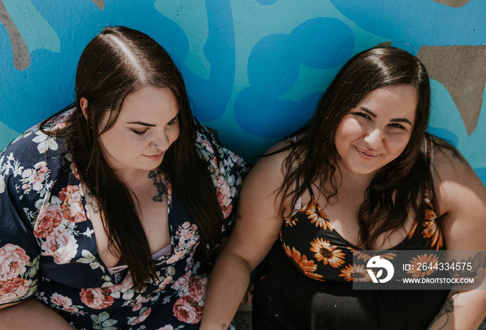 2 women sit against a blue background