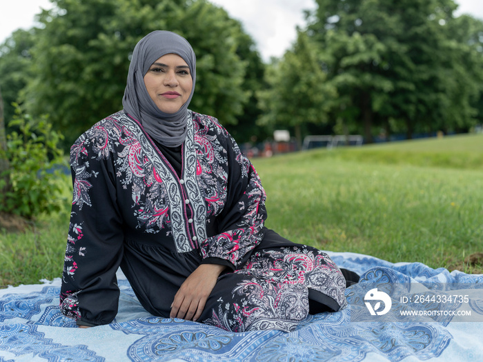 UK,Sutton,Portrait of woman in headscarf sitting on lawn in park