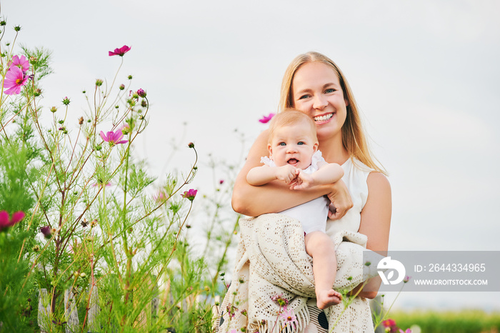 Happy young mother playing with baby girl in flower garden on a nice sunny day