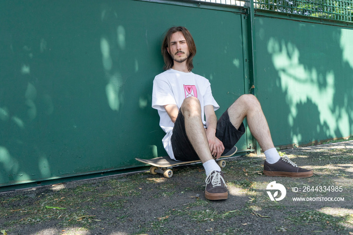 Portrait of young man sitting on skateboard in park