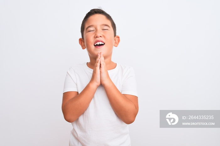 Beautiful kid boy wearing casual t-shirt standing over isolated white background begging and praying with hands together with hope expression on face very emotional and worried. Asking