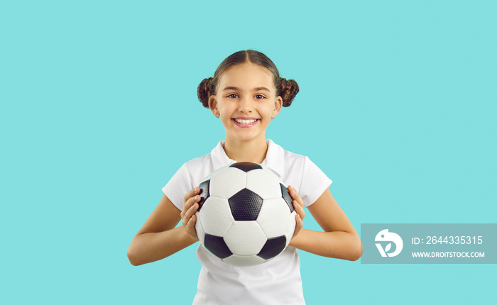 Portrait of smiling teen girl isolated on blue studio background hold ball cheer for sports team playing. Happy teenager child football fan excited about game or match. Hobby and activity.