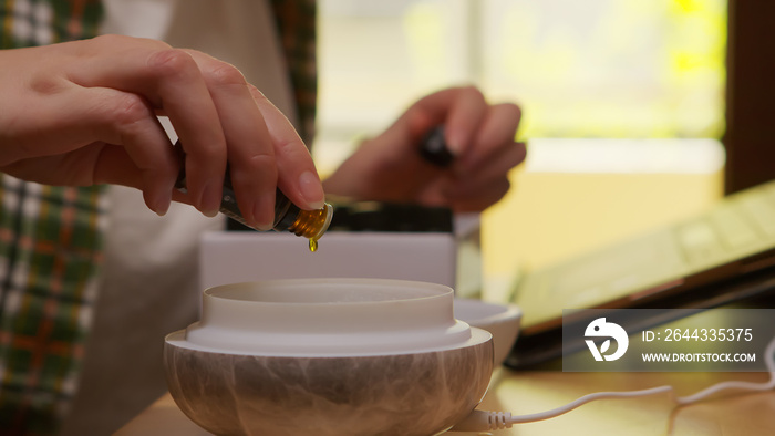 Woman adds essential oil into diffuser in kitchen