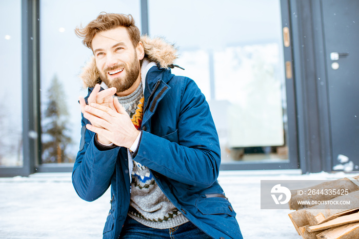 Portrait of a handsome man in winter clothes sitting on the terrace of the modern house