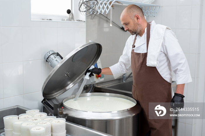 Cooking cheese from a private cheese factory. A man cuts raw materials with a large knife.