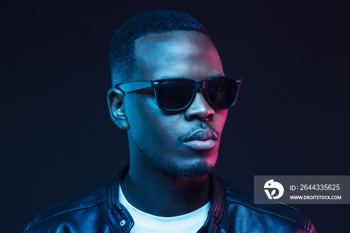 Neon studio portrait of african american male model wearing trendy sunglasses and leather jacket