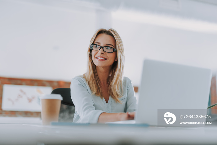 Positive businesswoman sitting with laptop and looking away