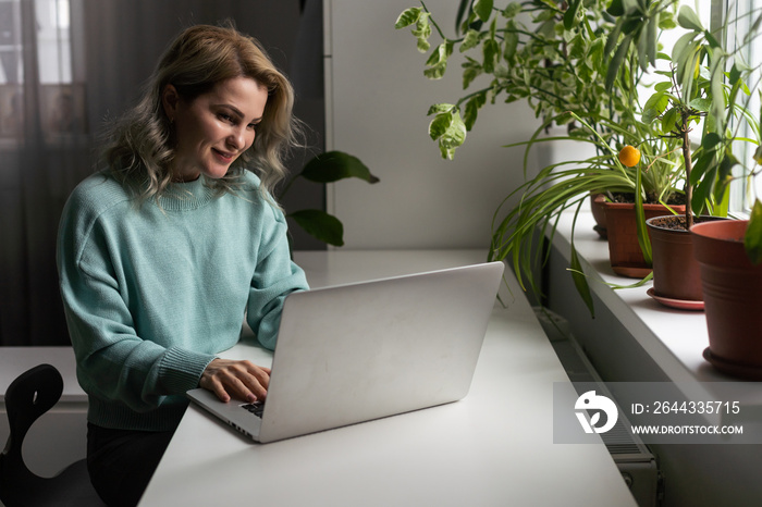 Young smiling happy satisfied employee business woman in casual blue shirt hold pen sit work at workplace white desk with laptop pc computer at light modern office indoors. Achievement career concept.