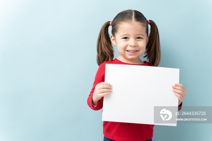 Portrait of a beautiful little girl with ponytails holding a white sign and smiling in a studio