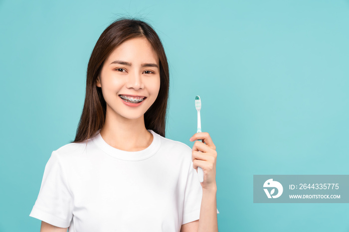 Smiling Asian woman holding toothbrush with braces on teeth isolated on blue background, Concept oral hygiene and health care.