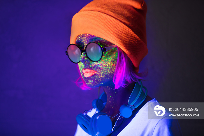 Young girl in hat with fluorescent paint on lips and face and headphones. Studio shot.