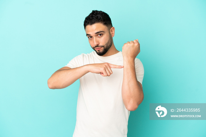 Young arab man isolated on blue background making the gesture of being late