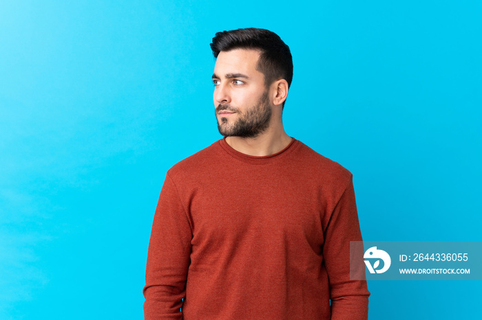 Young handsome man with beard over isolated blue background looking side