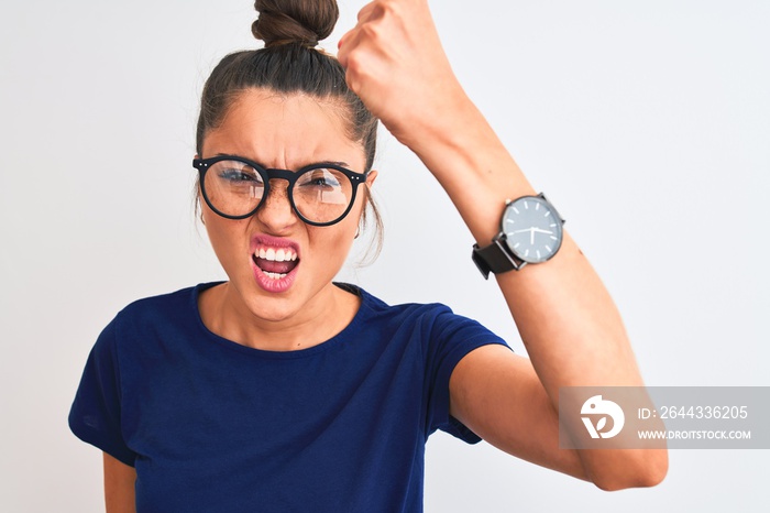 Beautiful woman with bun wearing blue t-shirt and glasses over isolated white background annoyed and frustrated shouting with anger, crazy and yelling with raised hand, anger concept