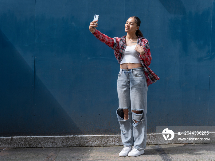 Young woman taking selfie against blue wall