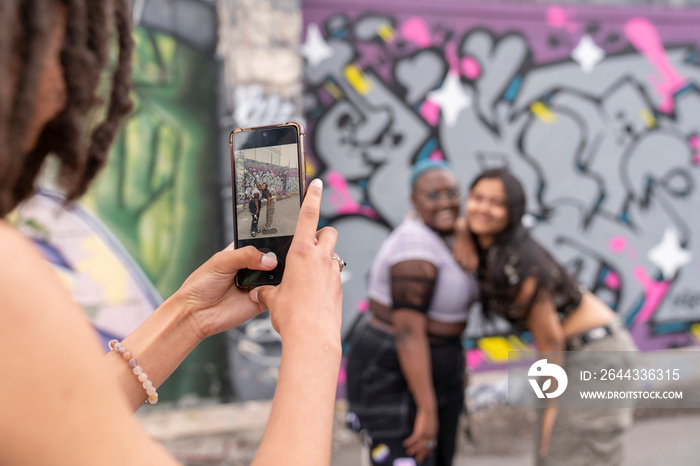 Woman photographing friends against graffiti wall