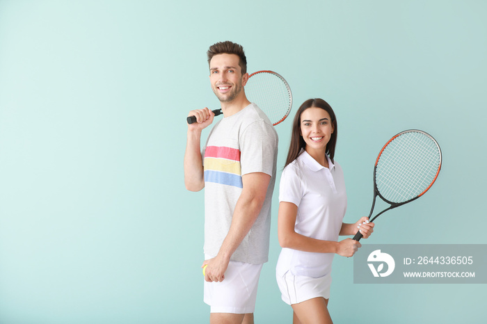 Young couple with tennis rackets on color background