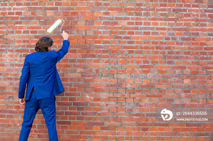 businessman in blue suit standing at brick wall with paint roller