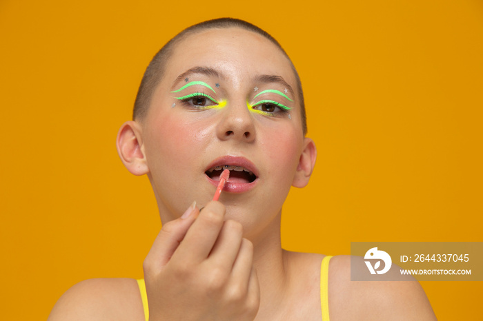 Studio portrait of girl with neon colored make-up applying lip gloss