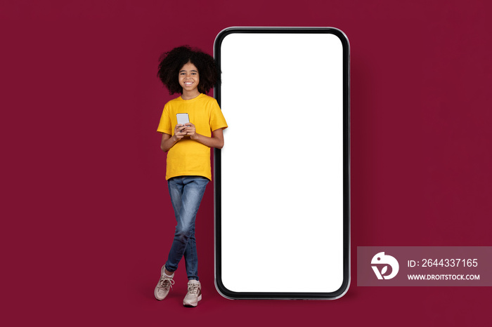 Positive african american girl standing by huge cell phone, mockup