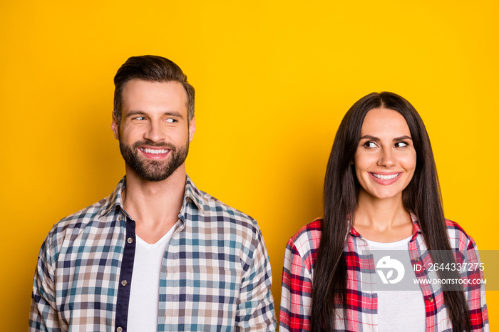 Portrait of two attractive cheerful people wear checked shirts looking at each other isolated over bright yellow color background