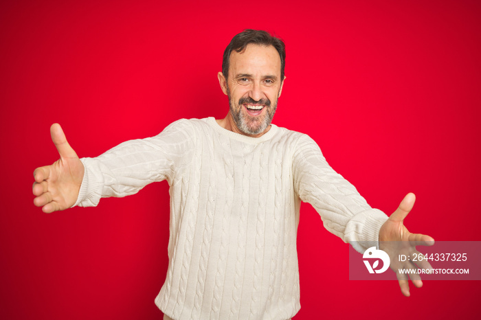 Handsome middle age senior man with grey hair over isolated red background looking at the camera smiling with open arms for hug. Cheerful expression embracing happiness.