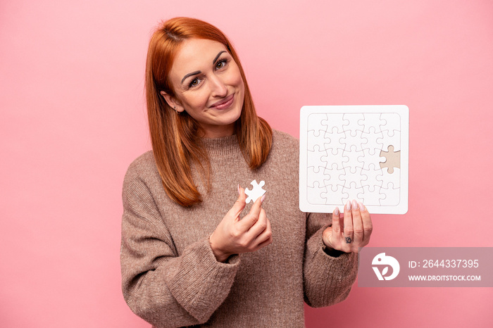 Young caucasian woman holding puzzle isolated on pink background