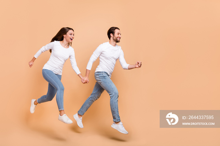 Full length body size view of attractive cheerful partners jumping holding hands going isolated over beige pastel color background