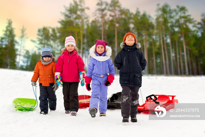 childhood, sledging and season concept - group of happy little kids with sleds in winter over forest background