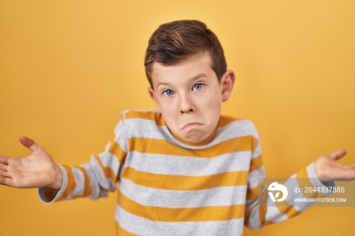 Young caucasian kid standing over yellow background clueless and confused expression with arms and hands raised. doubt concept.