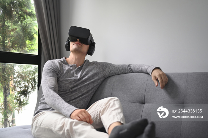 Young man  watching movie with virtual reality headset on couch at home.