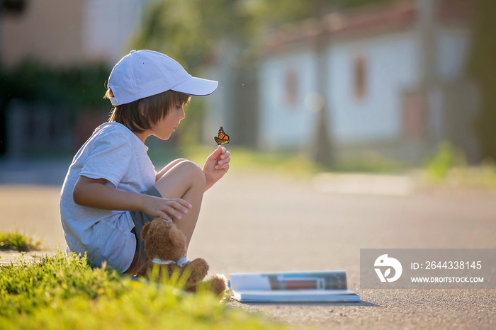 Beautiful kid boy, reading a book on the street, sitting down wi