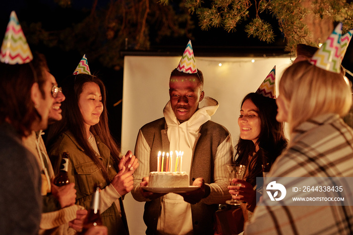 Young African man looking at candles on birthday cake while making wish