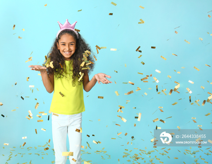 Cute African-American girl with crown and falling confetti on color background