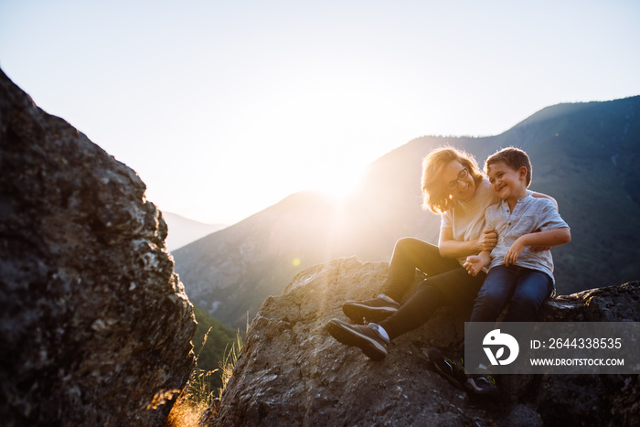 Mother and six-year-old son sitting on the mountain at sunset