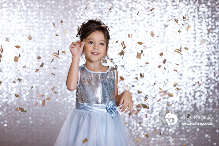 cute happy little child girl in princess blue dress dancing on confetti background with silver bokeh. birtday party