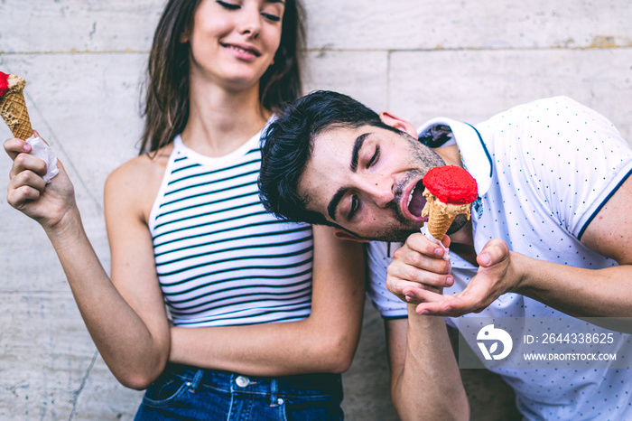 A young couple has fun joking and eating an ice cream that is starting to melt.