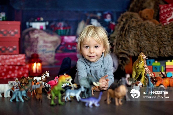 Sweet blonde toddler boy, playing with plastic animals and dinosaurs at home