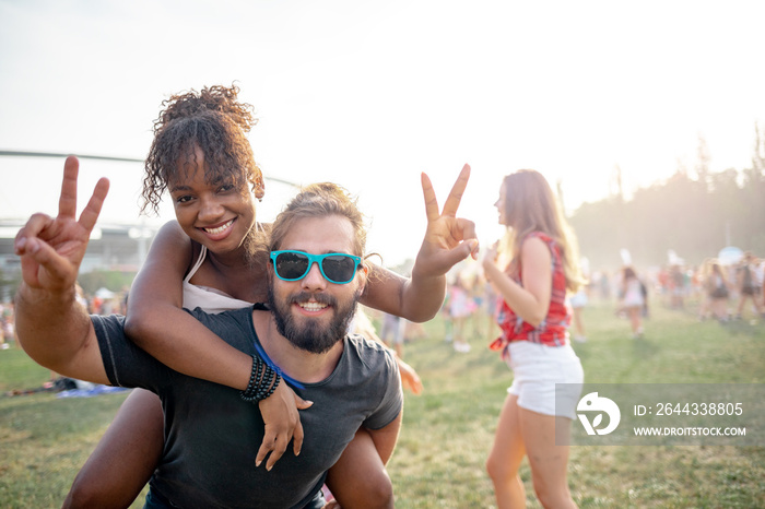 Portrait of multiethnic couple piggybacking at summer music festival