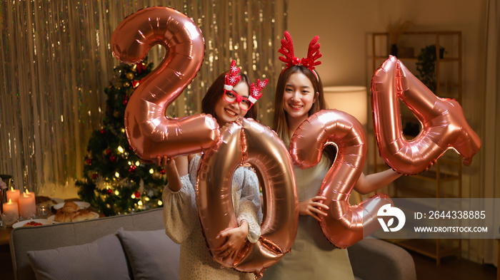 New Year celebration concept, Two beautiful women holding balloon pink gold number 2024 in party