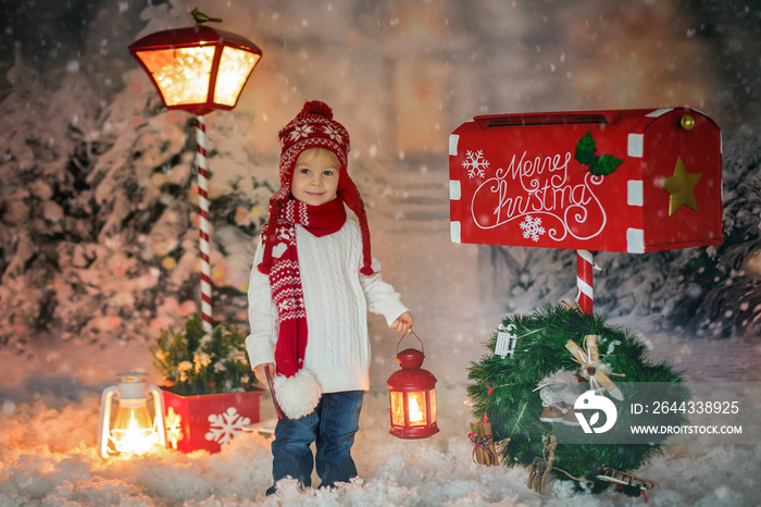 Little child, toddler boy, sending letter to santa in christmas mailbox, christmas decoration around him, outdoor shot